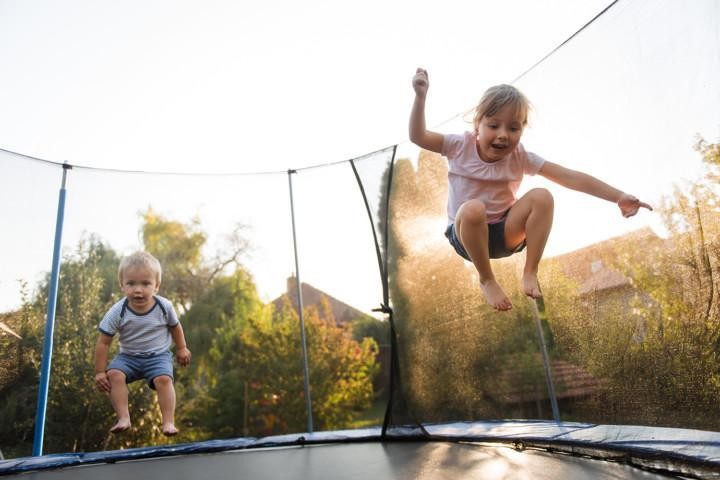 Kaksi pientä lasta pomppimassa trampoliinilla pihamaalla